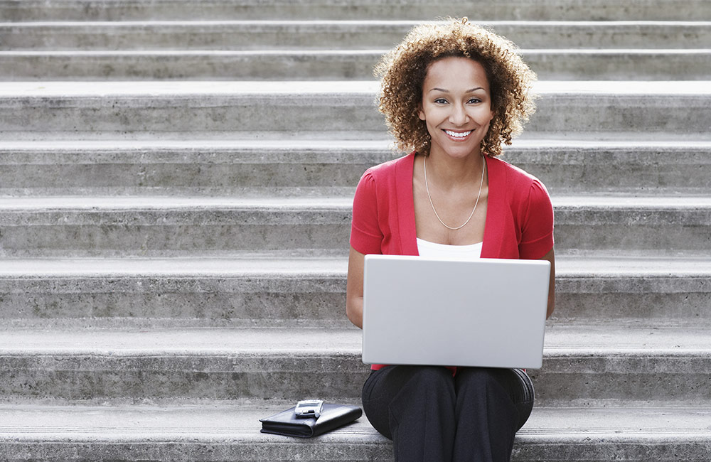 A happy woman sits with a laptop working on her resume