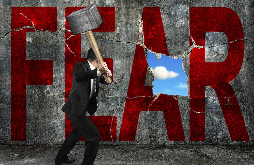 A man crushes through a wall with the word Fear painted on it